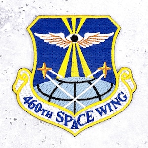 May include: A shield-shaped embroidered patch featuring a blue background with a central black circle, white wings, and yellow rays extending downward. Below, a light blue globe with black grid lines is crossed by two yellow stars. Text reads 460TH SPACE WING.