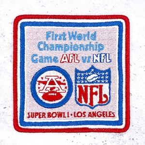 Puede incluir: Parche bordado con borde rojo, blanco y azul. El parche presenta el texto "First World Championship Game AFL vs NFL" y "Super Bowl I Los Angeles". También se incluyen los logotipos de la AFL y la NFL.