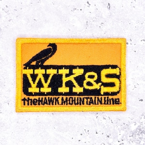 May include: Rectangular patch with an orange background and a black border. The patch features the text "WK&S" in yellow, with a black bird perched above. Below the text is "the HAWK MOUNTAIN Line" in black.