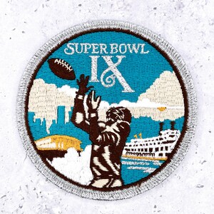 May include: A circular embroidered patch featuring the text SUPER BOWL IX in white. The design depicts a brown football player reaching up toward a brown football against a bright blue sky, with white clouds, a yellow stadium, and a white ship.