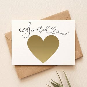 May include: A white scratch-off card with a gold heart shape, the words "Scratch Me!" in elegant script, and a brown envelope. The card is on a neutral background with a sprig of greenery.