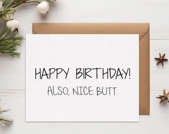 May include: A white greeting card with the text "HAPPY BIRTHDAY! ALSO, NICE BUTT." is displayed on a white wooden surface. The card is paired with a brown envelope. Decorative elements include pinecones and star-shaped ornaments.