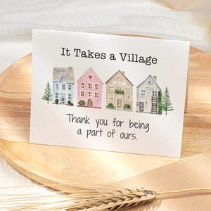 Op de afbeelding: Een wenskaart met de tekst "It Takes a Village" en "Thank you for being a part of ours." De kaart toont aquarel illustraties van vier kleurrijke huizen en twee kleine groenblijvende bomen.