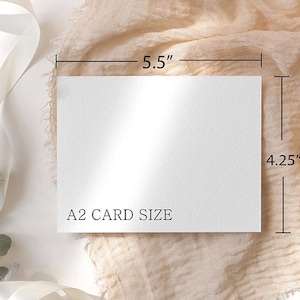 May include: A white A2 card, measuring 5.5 inches by 4.25 inches, is displayed on a beige fabric background. The card's dimensions are clearly marked with black lines and measurements. The text "A2 CARD SIZE" is printed on the card.