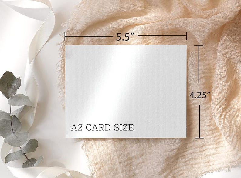 May include: A white A2 card, measuring 5.5 inches by 4.25 inches, is displayed on a beige fabric background. The card's dimensions are clearly marked with black lines and measurements. The text "A2 CARD SIZE" is printed on the card.