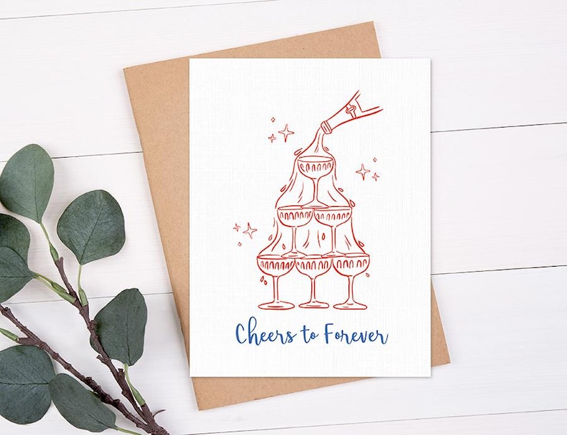 May include: A white greeting card with a red illustration of champagne glasses stacked in a pyramid shape, with a bottle pouring champagne. The words "Cheers to Forever" are written in blue.