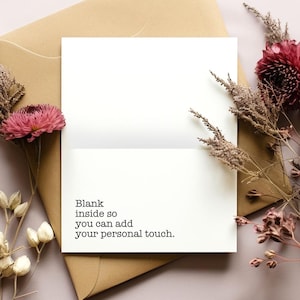 May include: A blank white greeting card with the text "Blank inside so you can add your personal touch." is placed on a brown envelope. The card is decorated with dried flowers and a pink flower.