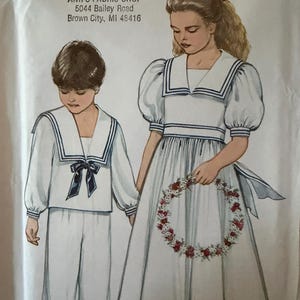 May include: New Look 6269 sewing pattern envelope featuring illustrations of two children in white sailor-style outfits with navy blue trim. The left figure wears a long-sleeved top and pants, while the right figure wears a puff-sleeve dress.
