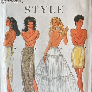 May include: Simplicity sewing pattern featuring illustrations of four different skirt styles. The pattern includes a long skirt with a slit, a floral print skirt, a tiered skirt, and a lace-trimmed skirt. The pattern size range is XS to XL.