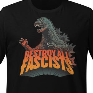 May include: Black t-shirt featuring a Godzilla-like monster with the text "DESTROY ALL FASCISTS" in orange and yellow. The monster is green and gray with red accents. The shirt is a short-sleeved crew neck.