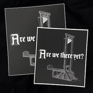 May include: Two black and white art prints featuring a guillotine illustration. One print displays the text "Are we" and the other reads "Are we there yet?" The prints have white borders and are set against a dark background.