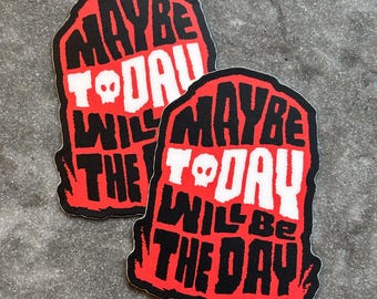 Pode incluir: Dois autocolantes com um design de lápide vermelha e preta. Os autocolantes têm o texto "MAYBE TODAY WILL BE THE DAY" em branco, com uma caveira substituindo o "O" em "TODAY".
