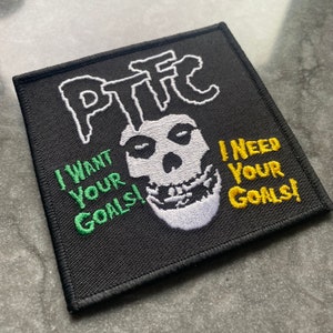 Op de afbeelding: Vierkant zwart embleem met wit, groen en geel geborduurd tekst en een schedelontwerp. De tekst luidt "PTFC", "I WANT YOUR GOALS!" en "I NEED YOUR GOALS!".