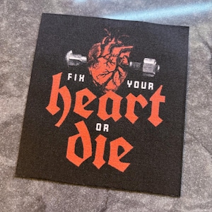 Könnte beinhalten: Schwarzer quadratischer Aufnäher mit den Worten "FIX YOUR heart OR DIE" in roter gotischer Schrift. Ein rotes anatomisches Herz und eine Langhantel befinden sich über dem Text.