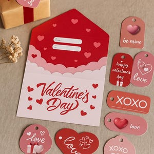 Puede incluir: Un conjunto tem&aacute;tico del D&iacute;a de San Valent&iacute;n con un sobre rojo, etiquetas de regalo y un regalo envuelto. El sobre es rojo con un interior blanco y detalles de coraz&oacute;n. Las etiquetas de regalo incluyen dise&ntilde;os "be mine", "XOXO" y "love". El regalo est&aacute; envuelto en papel marr&oacute;n con un lazo rojo.