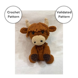 May include: A crocheted Highland cow plushie in shades of brown, tan, and black. The handmade stuffed animal features a shaggy mane, horns, and a round body. The image includes text that says "Crochet Pattern" and "Validated Pattern".