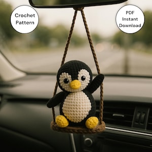 May include: A handmade crocheted penguin car charm in black, white, and yellow, hanging from a brown string. The penguin is sitting on a brown swing. Text on the image reads "Crochet Pattern" and "PDF Instant Download".