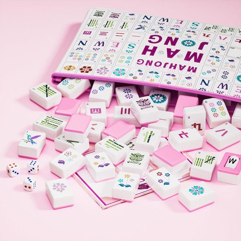 May include: A Mahjong set featuring white tiles with colorful floral, bamboo, and character designs, along with three white dice. The tiles are scattered in front of a white zippered storage case printed with the text MAH JONG SEWN in purple.