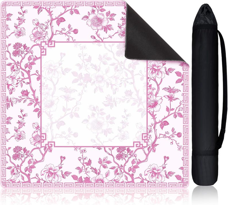 May include: A square mat featuring a pink and white floral pattern with a geometric border and a central blank rectangular space. The mat has a black underside and is shown alongside a black cylindrical carrying case with a shoulder strap.