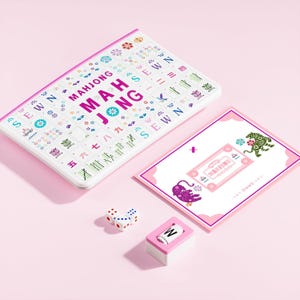 May include: A Mahjong game set featuring a white rectangular board with colorful printed tiles, text reading MAHJONG, and the word SEWN. Includes a rectangular instruction card with tiger illustrations, three white dice, and a single letter W tile.