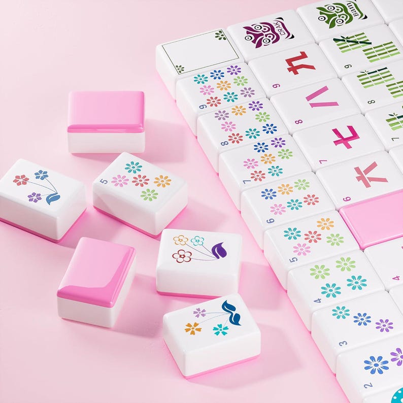 May include: A set of white and pink mahjong tiles featuring colorful floral patterns, bamboo designs, and Chinese characters. Some tiles are arranged in a grid, while others are scattered, displaying various numbers and decorative motifs.