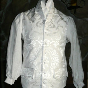 May include: A white brocade vest with a high collar and a white shirt underneath. The vest has a floral pattern and is buttoned up the front.
