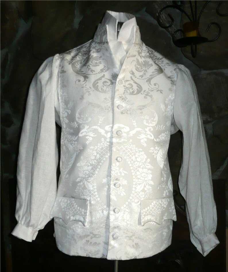 May include: A white brocade vest with a high collar and a white shirt underneath. The vest has a floral pattern and is buttoned up the front.