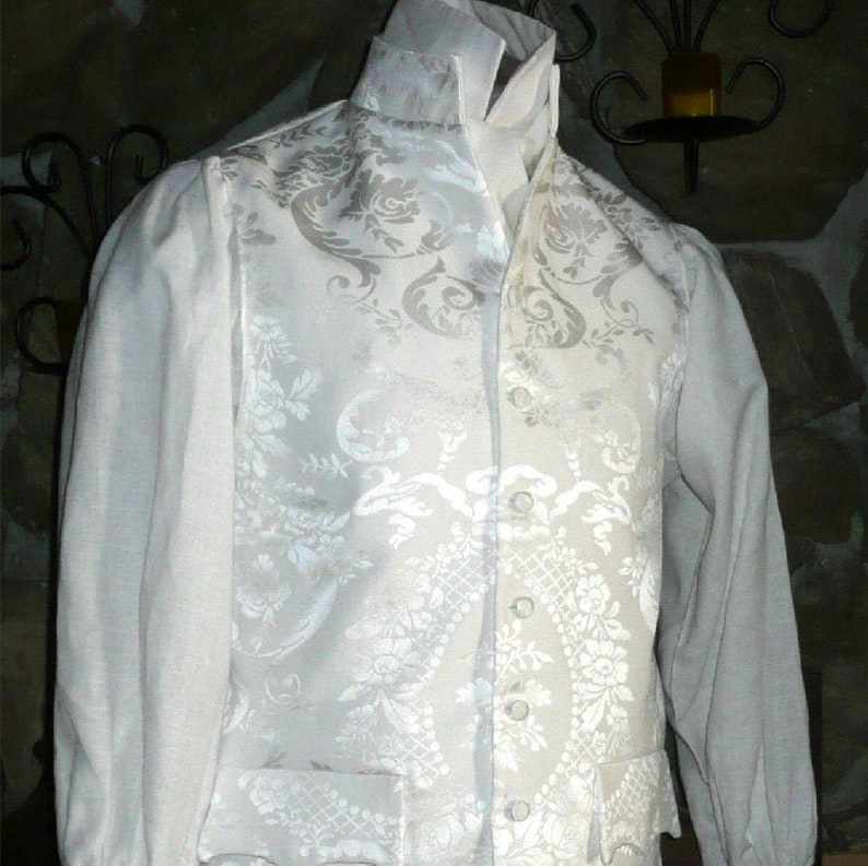 May include: A white vest with a white floral pattern. The vest has a high collar and a button-up front.