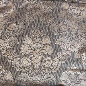 May include: A close-up of a fabric with a gold and brown damask pattern. The fabric has a subtle sheen and a textured surface.