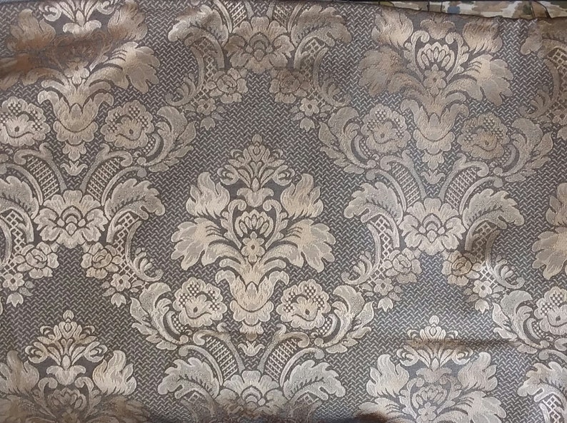 May include: A close-up of a fabric with a gold and brown damask pattern. The fabric has a subtle sheen and a textured surface.