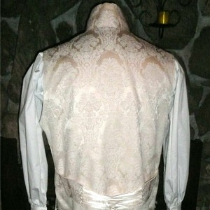 May include: A white brocade vest with a white satin back and a white shirt with long sleeves and ruffled cuffs.