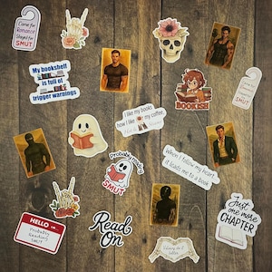 Puede incluir: Una colección de pegatinas con temática de lectura, con frases como "Read On", "Just one more chapter" y "Probably reading SMUT". Las pegatinas incluyen ilustraciones de un fantasma leyendo, una calavera con flores y figuras masculinas.