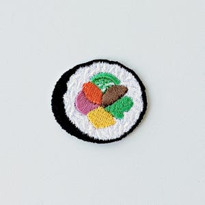 Könnte beinhalten: Gestickter Sushi-Aufnäher mit einer farbenfrohen Füllung aus Orange, Rosa, Gelb, Grün und Braun. Die Sushi-Rolle ist von weißem Reis und einem schwarzen Nori-Algen-Rand umgeben. Ein lustiges Accessoire zum Thema Essen.