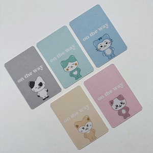May include: A collection of rectangular cards in various pastel colors, each featuring a cartoon animal character and the text "on the way." The characters include a cat, a bear, a fox, and other stylized creatures. The cards are arranged on a white surface.