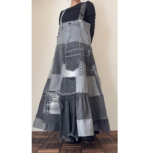 Puede incluir: Un vestido de peto de mezclilla patchwork en tonos grises y negros. El vestido presenta una parte superior de peto con tirantes ajustables y una falda completa y fluida construida a partir de varios parches de mezclilla. El dobladillo tiene un borde deshilachado.