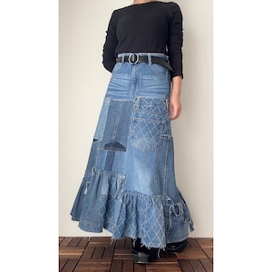 Peut inclure: Longue jupe en jean avec un design patchwork. La jupe présente différentes nuances de denim bleu, avec des poches et un ourlet à volants. Une ceinture noire cintre la taille. La jupe est associée à un haut noir à manches longues et à des bottes à plateforme noires.