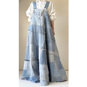 Puede incluir: Vestido de peto vaquero patchwork en varios tonos de azul. El vestido presenta una falda amplia y tirantes ajustables. La prenda está hecha de mezclilla reciclada y tiene una apariencia única y artesanal.
