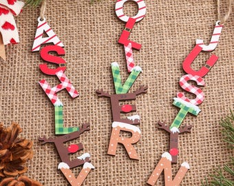 May include: Wooden Christmas ornaments spelling out "Ashley", "Love", and "Justin". The letters are decorated with red and white stripes, red and white gingham, and green plaid patterns. The ornaments hang from twine.