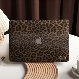 Op de afbeelding: Een laptopskin met een bruin en zwart luipaardpatroon, voorzien van een zilverkleurig Apple-logo in het midden en de goudkleurige initialen C.A. in de rechterbenedenhoek, aangebracht op de deksel van een gesloten laptop.