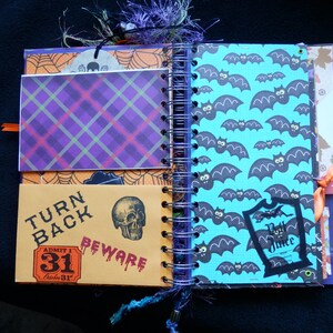 May include: Open Halloween journal with spiral binding. Pages feature plaid, bat, and skull patterns. Text includes "Turn Back Beware" and "Admit 1 October 31". Orange and purple accents.