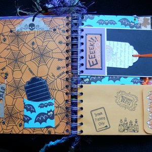 May include: Halloween scrapbook open to a double-page spread. One page has an orange spiderweb design, the other a blue bat pattern. Includes tags, pockets, and the text "EEEK!!" and "Witches Brew". Features a "Broom Parking Only" sign.