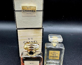 May include: Two Chanel No. 5 perfume bottles and two boxes. One bottle is filled with orange liquid, the other is empty. The boxes and bottles have the Chanel logo and "N°5" printed on them.