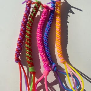 Puede incluir: Cinco llaveros trenzados de colores en tonos rojos, verdes, rosas, azules y amarillos. Cada llavero tiene un lazo en el extremo. Los llaveros están hechos de un material flexible similar al plástico.