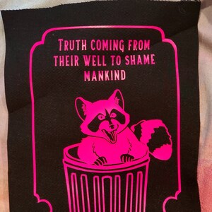 May include: A black patch with a pink border and a pink raccoon inside a pink trash can. The text "TRUTH COMING FROM THEIR WELL TO SHAME MANKIND" is written in pink.