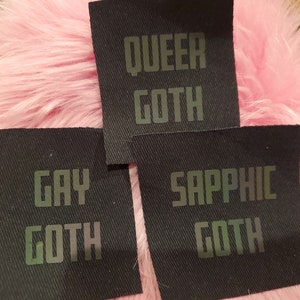 Może przedstawiać: Trzy czarne łatki z tkaniny z iryzującym zielonym tekstem. Łatki głosiły "Queer Goth", "Gay Goth" i "Sapphic Goth".