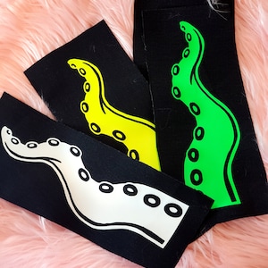 May include: Three black fabric patches with different colored octopus designs. The octopus on the left is white, the middle octopus is yellow, and the octopus on the right is green.