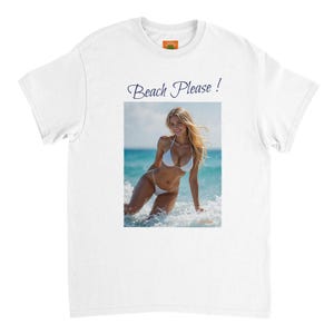 Pode incluir: Camiseta branca com uma fotografia de uma mulher de biquíni branco na praia. O texto "Beach Please!" é impresso acima da fotografia em uma fonte cursiva. A camisa tem gola redonda e mangas curtas.