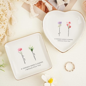 May include: Two white ceramic trinket dishes with gold-toned rims. One dish is square, the other heart-shaped. Both feature floral illustrations, the names Dallas, Allison, Evelyn, and Marian, and the text IF FRIENDS WERE FLOWERS I WOULD PICK YOU.