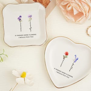 May include: Two white ceramic trinket dishes with gold-toned rims. One dish is square with rounded corners, the other is heart-shaped. Both feature floral illustrations, personalized names, and the text IF FRIENDS WERE FLOWERS I WOULD PICK YOU.