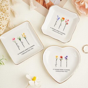 May include: Three white ceramic trinket dishes with gold-toned rims in square, scalloped, and heart shapes. Each dish features watercolor-style floral illustrations, personalized names, and the printed text: IF FRIENDS WERE FLOWERS I WOULD PICK YOU.
